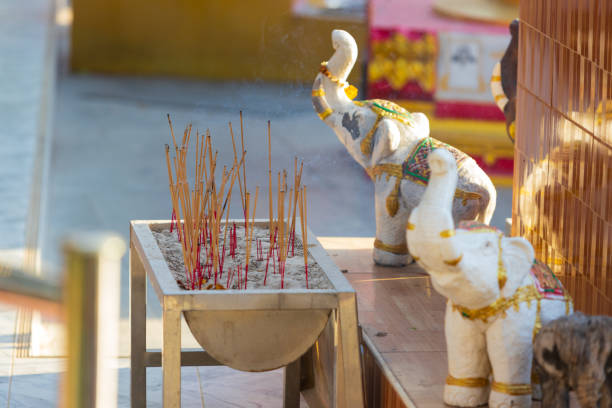 Buddhist altar with many smoking aroma incense sticks in front of blurred small elephant statues at temple. Burning incense sticks outdoors at Buddhist wat. Offering for the deities at Thailand.