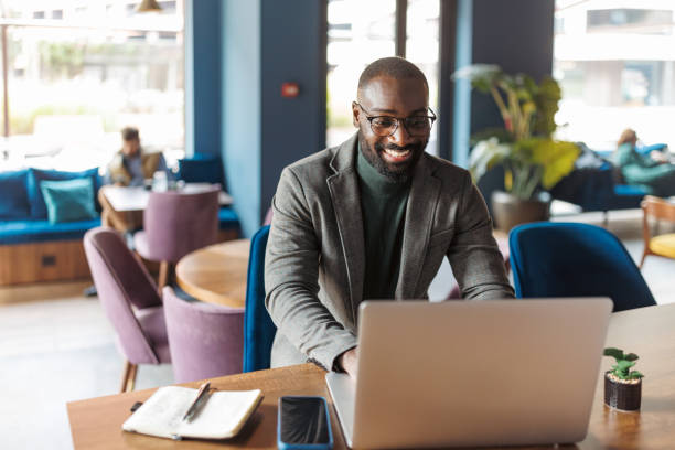 istock Smiling man with laptop in modern cafe setting. 2183841186