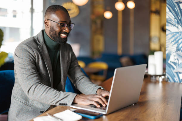 Man smiling while typing on laptop in cozy cafe.
