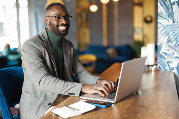 istock Man smiling as he types at laptop in bright cafe. 2183841364