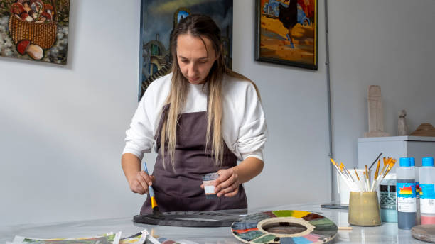 istock In an art studio with an environment adorned with artistic paintings in the background, a beautiful middle-aged woman is painting a clay ceramic frame black at a table 2183843025