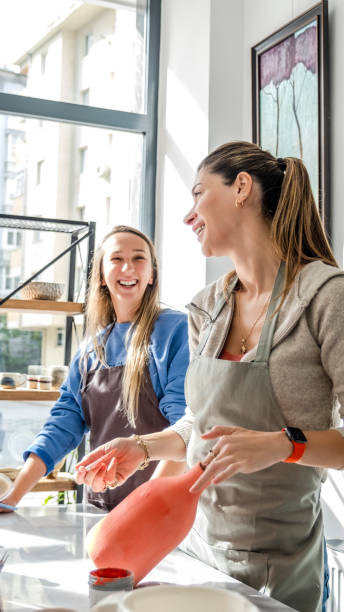 istock In an art studio with an environment adorned with artistic paintings in the background, two beautiful middle-aged women are joyfully painting a clay ceramic vase pink together at a table, having fun 2183843323