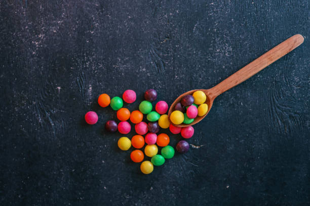istock A wooden spoon overflowing with vibrant, multicolored candy spheres against a textured dark background. The colorful arrangement adds a playful contrast to the rustic setting, creating a visually appealing composition 2183845536