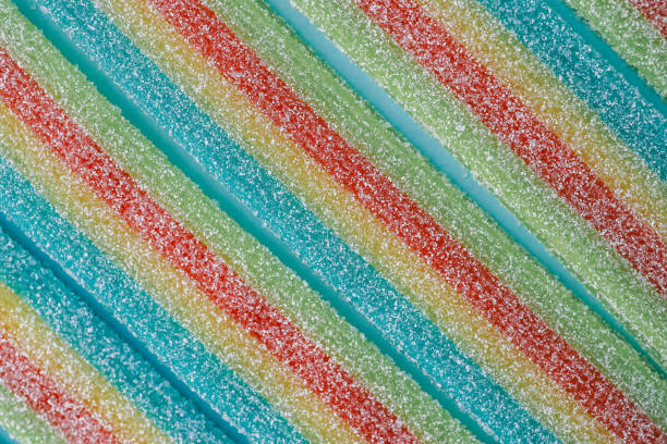 Colorful sugar-coated rainbow candy strips laid in parallel rows on a light blue background. The vibrant colors and texture highlight the sugary details, making it perfect for sweet and festive themes.