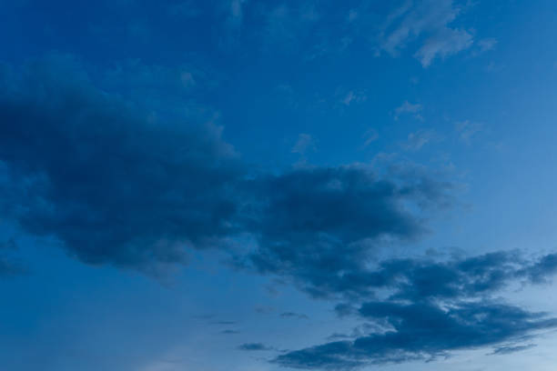 Dark fluffy clouds drift across a vibrant blue summer sky