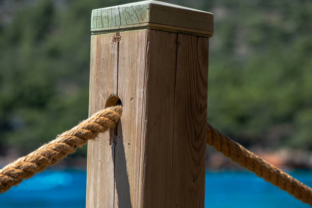 A close-up of a wooden post with a rope, set against clear blue ocean waters, evokes coastal vibes and tranquility, perfect for nautical or seaside themes and concepts.