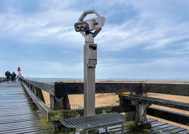 A coin-operated binoculars showing the sandy Playa de las Arenas beach in Valencia, Spain on a sunny day with beachgoers and the sea