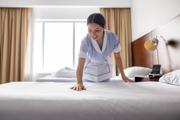 Happy Latin American housekeeper making the bed in a hotel room while smiling - service occupation concepts