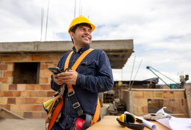 construction worker smiling and using his cell phone at a building site - byggarbetare bildbanksfoton och bilder
