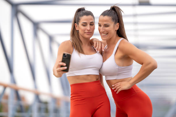 Two friends taking selfie together on bridge after workout, both in matching activewear.