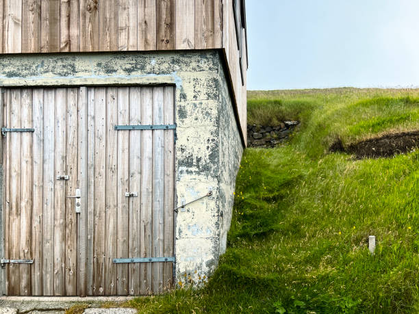 Old wooden barn, shed, home or boathouse built into the side of a lush green mountain. Located in the remote Scandinavian island of Nólsoy within the Faroe Islands.