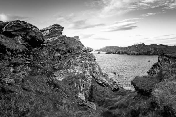 A tranquil coastal view showcases rugged cliffs and calm waters at dusk. The scene captures the contrast of shadows and light against the rocks, creating a serene atmosphere.