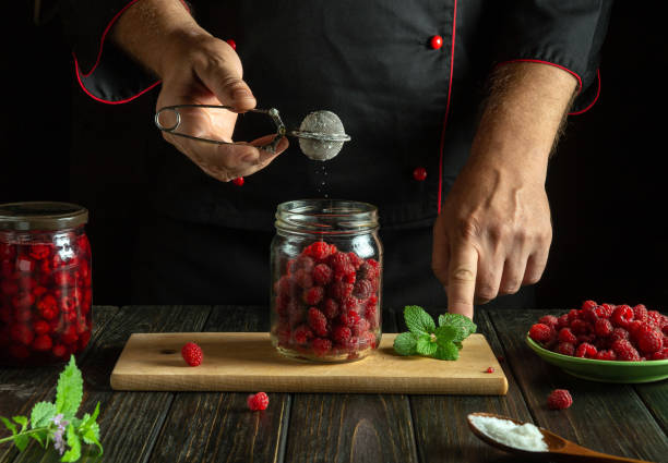 istock A chef skillfully uses a sieve to sprinkle sugar over a jar filled with fresh raspberries. Mint leaves and extra berries are arranged on the table, creating a warm, inviting atmosphere 2183876471