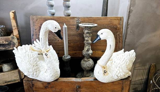 Two white swan statues sit side by side on a wooden chest. A candle and a candlestick are placed between them, creating a romantic atmosphere.