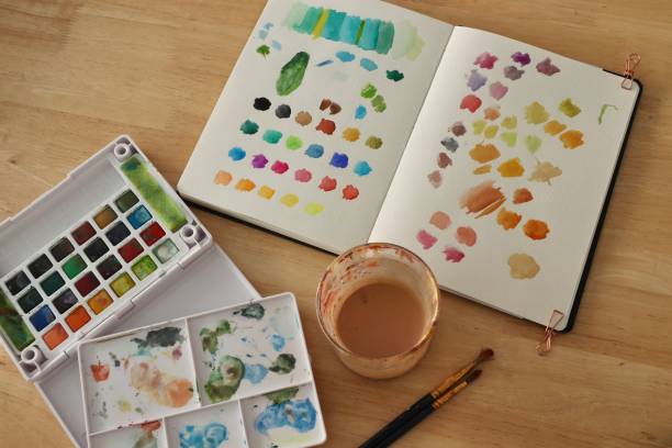 istock Artistic Workspace with Portable Watercolor Set, Colorful Swatch Testing, and Rinse Cup on Wooden Table 2183886632