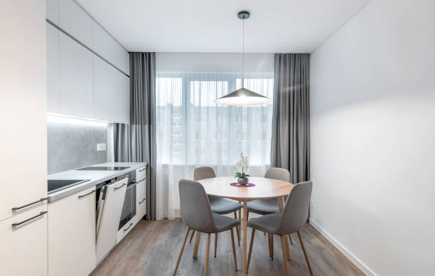 Classic Bright Home Kitchen Interior and Dining Table. Oven, Windows. Dinning Table and Chairs. Minimalistic Scandinavian Interior Design. LED Lights, Hardwood Floor. White Walls.
