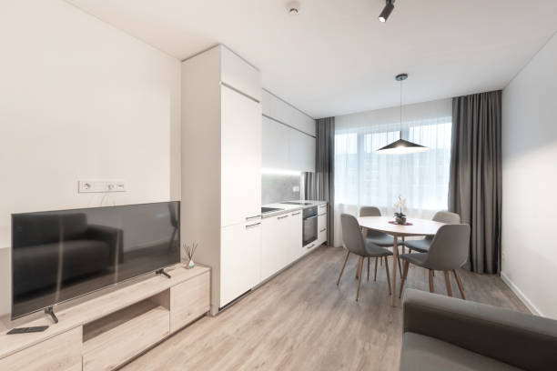 istock Classic Bright Home Living Room and Kitchen Interior Dining Table. Oven, Windows. Dining Table and Chairs. Couch Sofa and TV. Scandinavian Design. LED Lights, Hardwood Floor. White Walls. 2183895221