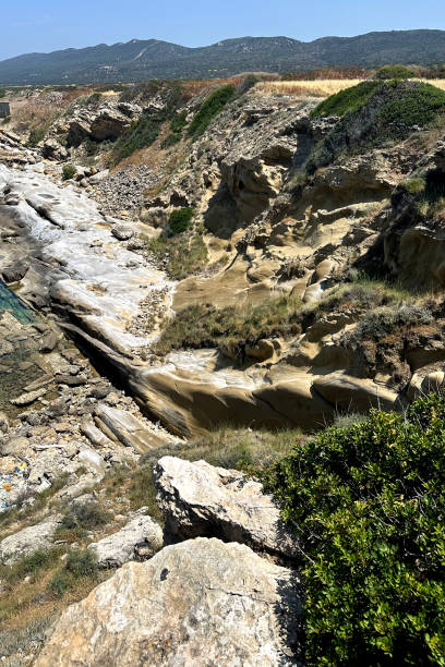 istock This scenic coastline features rocky cliffs, smooth erosion patterns, and patches of greenery. The area basks under bright sunlight against a backdrop of distant hills 2183897342