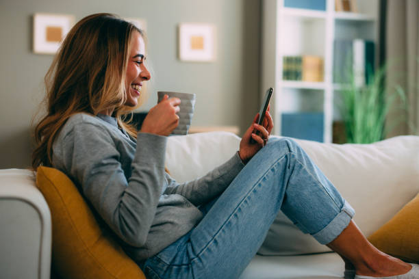 istock Happy woman relaxing on sofa drinking coffee and using smartphone 2183898146