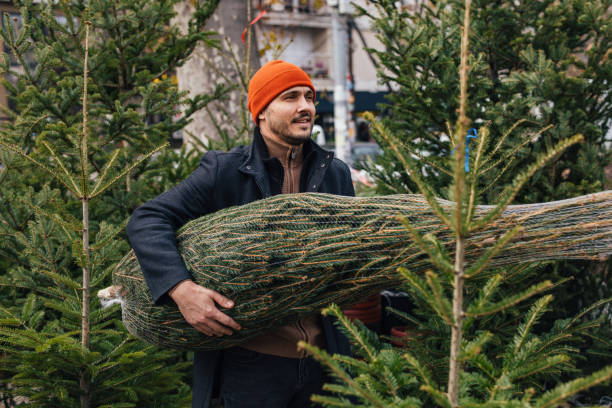 istock Man Carrying Christmas Tree Through Festive Market Setting 2183898449