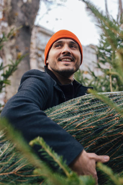 istock Smiling Man Carrying Christmas Tree Outdoors in Winter Attire 2183898461
