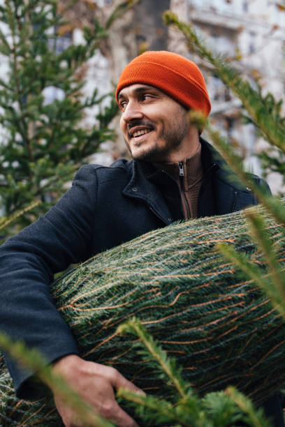 istock Man Smiling While Carrying Christmas Tree in Outdoor Urban Setting 2183898476