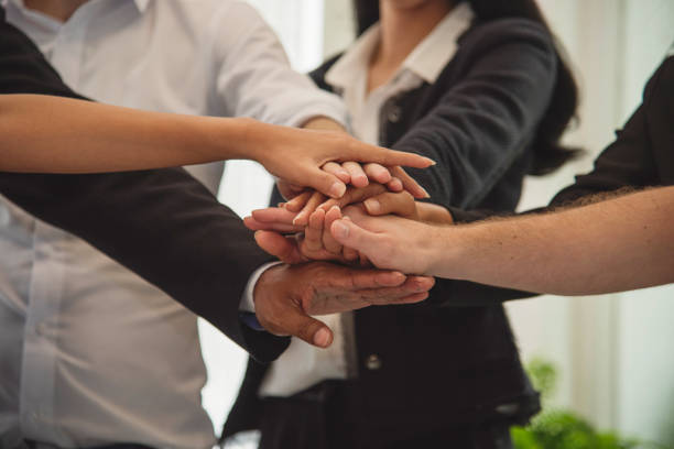 A group of business coworkers uniting their hands in a symbolic gesture of teamwork, representing cooperation and shared goals in a formal business setting