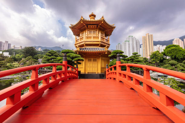 istock Pagoda and arched bridge. Trees, city skyline in background. Clouds overhead. 2183921209