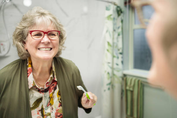 Senior Woman Brushing Teeth in a Modern Bathroom Mirror Reflection