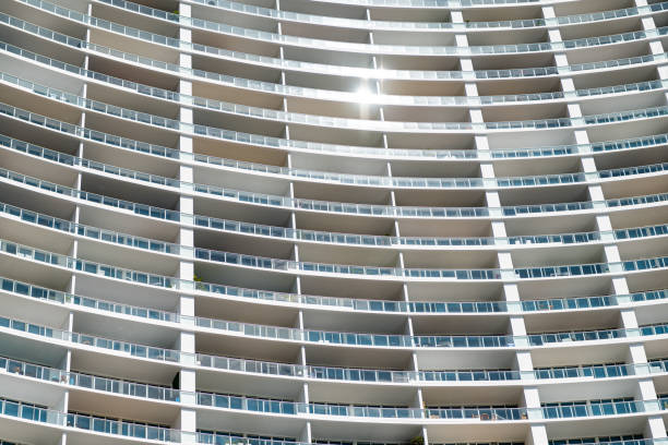 Facade of a glass building displaying a pattern of balconies, forming an abstract background with reflections of the sky and clouds.