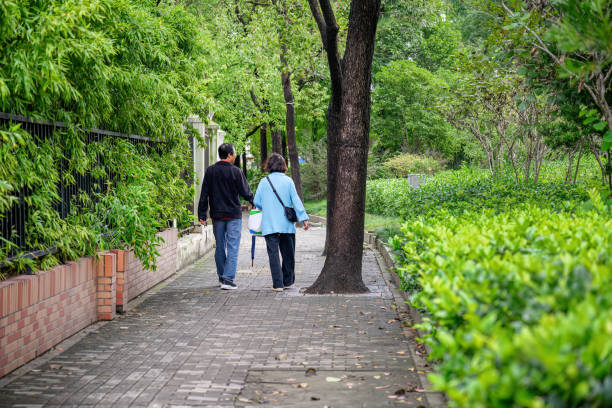 People walking on pavement among green trees.