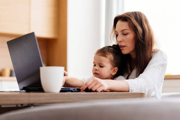 istock A woman works at a kitchen table with a laptop and a child 2183945384