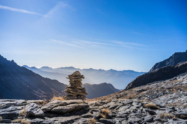 mountain path marker built with stones, mountain ranges in the background, clear blue sky