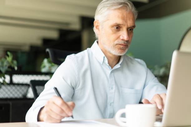 istock Smiling 40s male business man accountant analyst holding documents, work at laptop computer doing online trade research 2183968947