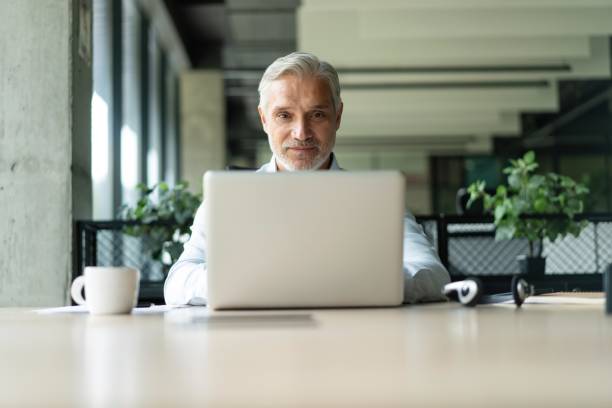 istock Happy mature professional business man looking at camera sitting at work desk using computer 2183969003