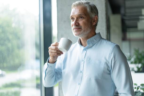 istock Smiling Middle Aged Businessman Standing In Office Setting With Coffee Mug. 2183969040