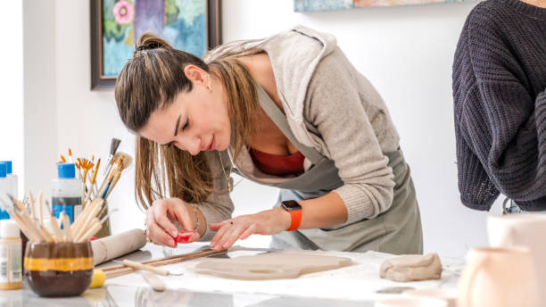 istock In an art studio with an environment adorned with artistic paintings in the background, a beautiful middle-aged woman artist is shaping clay with a wet sponge at a table 2183971820