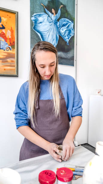 istock In an art studio with an environment adorned with artistic paintings in the background, a beautiful middle-aged woman artist is shaping clay with her hands at a table 2183971867
