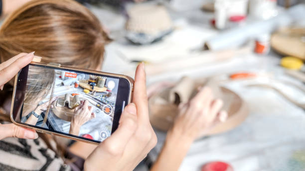 istock In an art studio with an environment adorned with artistic paintings in the background, a beautiful middle-aged woman artist is shaping clay at a table, while a young woman next to her is taking a photo with her phone 2183982270