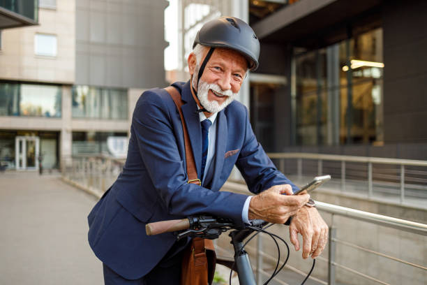 istock Portrait of optimistic senior commuter in helmet using mobile phone and standing with bicycle in city 2183988391