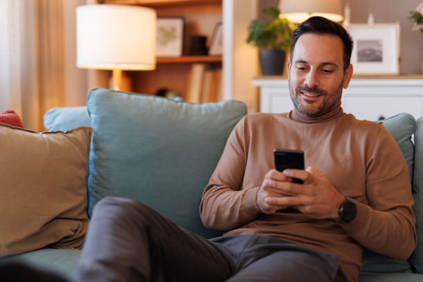 istock Portrait of confident handsome man text messaging over smart phone while relaxing on sofa in home office 2183988502