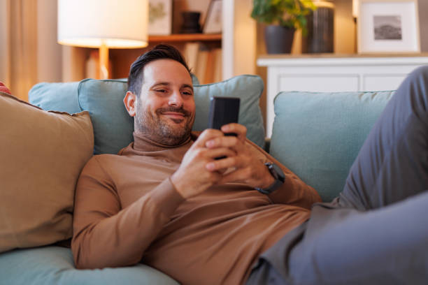 istock Smiling mid adult man using social media apps over smart phone while lying on cozy sofa in living room 2183988524
