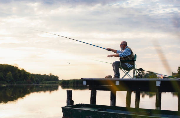 istock Elderly Man Fishing by Tranquil Lake at Sunset 2183990773