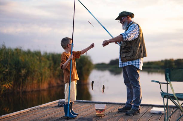 A grandfather and grandson enjoy a peaceful fishing trip on a wooden dock by the lake at sunset, creating precious family memories.