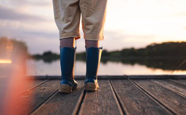 A child wearing blue boots stands on a wooden dock by the lake at sunset, suggesting adventure and tranquility in nature. The peaceful scene captures the essence of a serene lakeside moment.