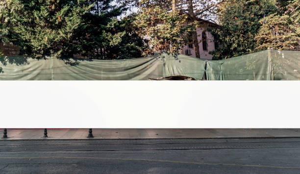 istock White banner stretched across construction site with green mesh fencing, trees and sidewalk in urban setting, ideal for signage or advertising mockups 2183991506