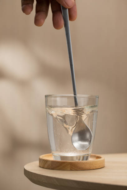 A hand stirs water in a glass with a spoon, mixing Himalayan salt. This blend is used during intermittent fasting for its health benefits, providing essential minerals and aiding in detoxification.