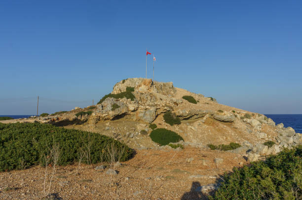 istock A rocky hill adorned with national flags overlooking a serene coastal landscape during sunset. 2183997240