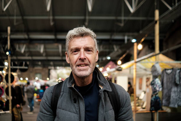 istock Grey-haired man smiling in a crowded indoor market wearing a backpack 2183998497