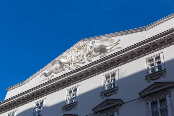 Triangular pediment on top of a building facade with white sculptures and stucco in a tympanum in the inner city of Vienna against the clear blue sky, Austria